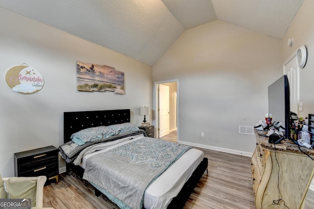 bedroom featuring vaulted ceiling, light hardwood / wood-style floors, and a textured ceiling