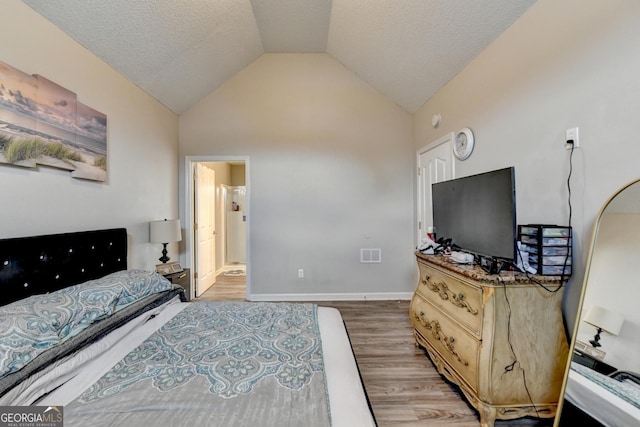 bedroom with ensuite bath, vaulted ceiling, a textured ceiling, and light wood-type flooring