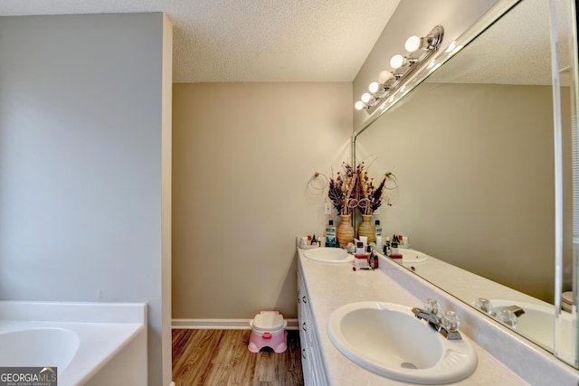 bathroom with hardwood / wood-style flooring, vanity, a tub, and a textured ceiling