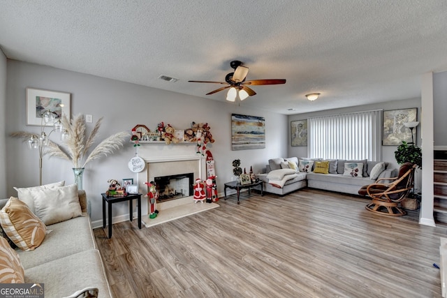 living room featuring ceiling fan, wood-type flooring, a high end fireplace, and a textured ceiling