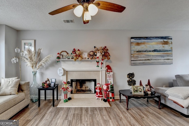 living room featuring hardwood / wood-style floors, a fireplace, a textured ceiling, and ceiling fan