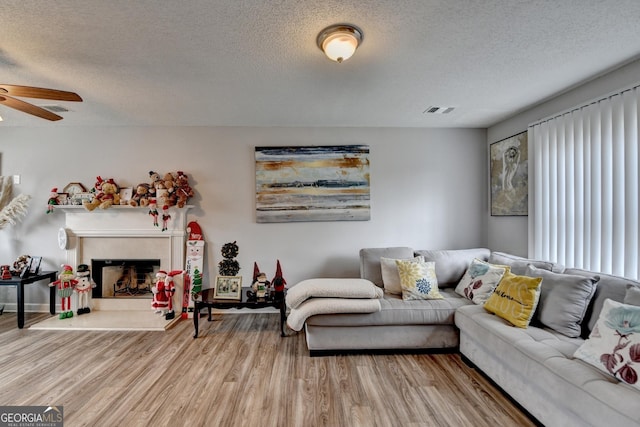 living room with a tiled fireplace, ceiling fan, hardwood / wood-style flooring, and a textured ceiling