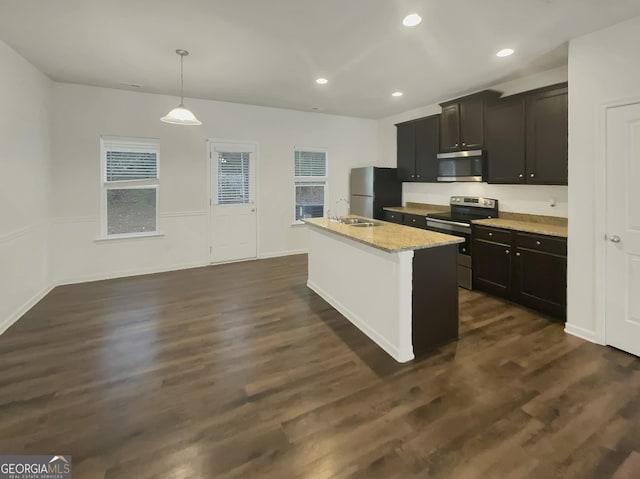 kitchen featuring dark wood-type flooring, decorative light fixtures, a center island with sink, stainless steel appliances, and light stone countertops