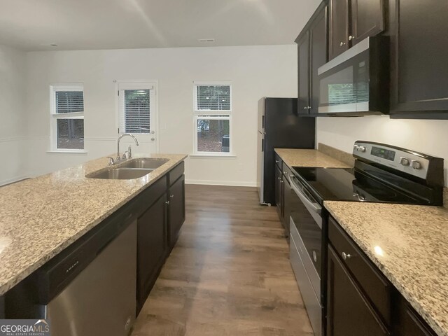 kitchen with sink, dark brown cabinetry, light stone counters, stainless steel appliances, and dark wood-type flooring