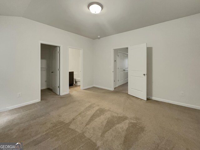 unfurnished bedroom featuring ensuite bath, vaulted ceiling, a walk in closet, light colored carpet, and a closet