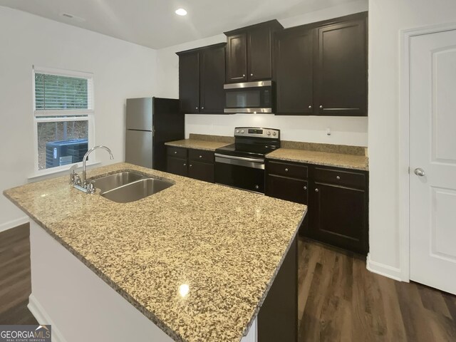 kitchen with light stone counters, appliances with stainless steel finishes, sink, and a kitchen island with sink