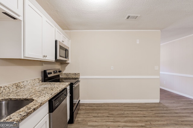 kitchen with appliances with stainless steel finishes, white cabinetry, wood-type flooring, light stone countertops, and a textured ceiling