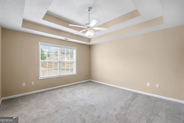 empty room with ceiling fan, a tray ceiling, carpet floors, and a textured ceiling