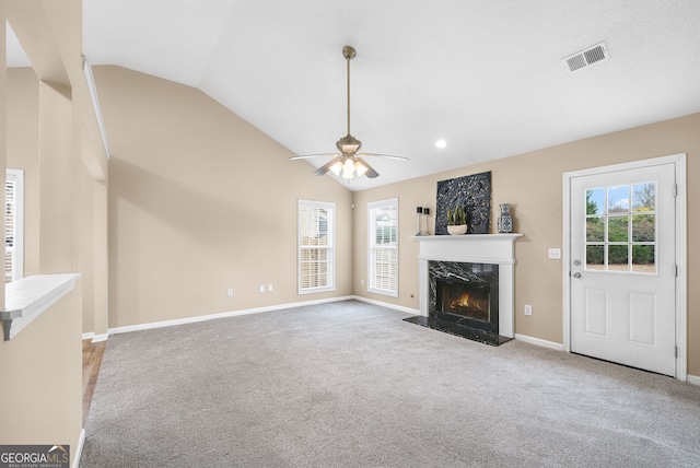 unfurnished living room with vaulted ceiling, a wealth of natural light, light colored carpet, and a high end fireplace