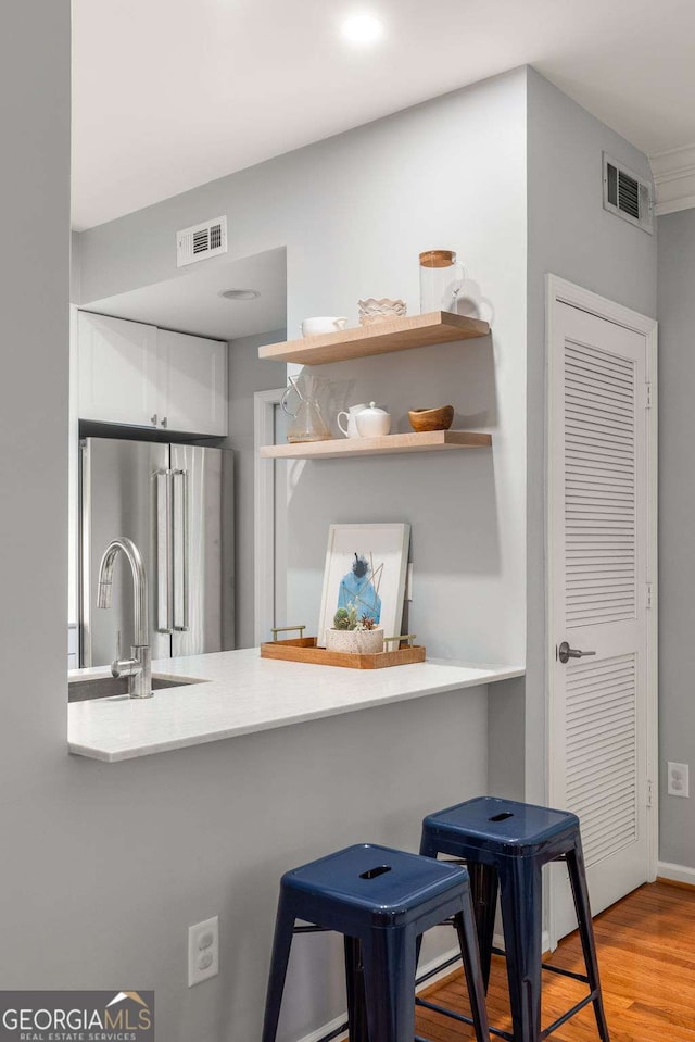 kitchen featuring sink, a kitchen breakfast bar, kitchen peninsula, high end fridge, and light wood-type flooring