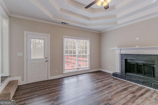 unfurnished living room featuring dark hardwood / wood-style flooring, a brick fireplace, a tray ceiling, and ornamental molding