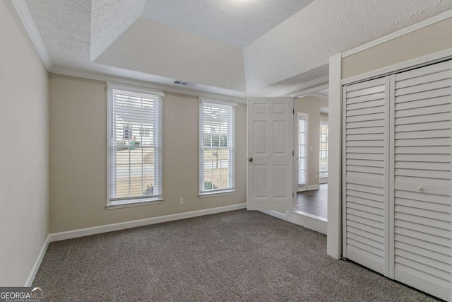 unfurnished bedroom with carpet, a tray ceiling, ornamental molding, a textured ceiling, and a closet