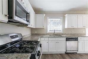 kitchen with appliances with stainless steel finishes, white cabinetry, sink, light stone countertops, and dark wood-type flooring