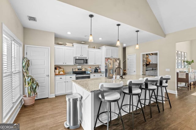 kitchen featuring a kitchen bar, white cabinetry, decorative light fixtures, stainless steel appliances, and a kitchen island with sink