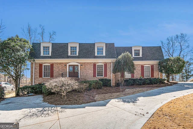 front of property featuring brick siding and roof with shingles