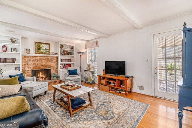 living area with visible vents, built in features, beamed ceiling, light wood-type flooring, and a brick fireplace