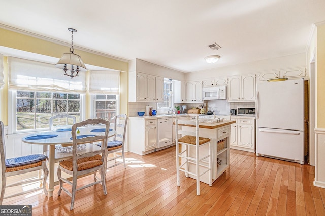 kitchen featuring light countertops, decorative backsplash, ornamental molding, white cabinets, and white appliances