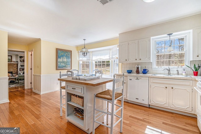 kitchen featuring a wainscoted wall, white cabinets, light wood-type flooring, dishwasher, and a kitchen breakfast bar