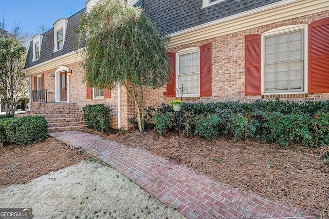 entrance to property featuring mansard roof, roof with shingles, and brick siding