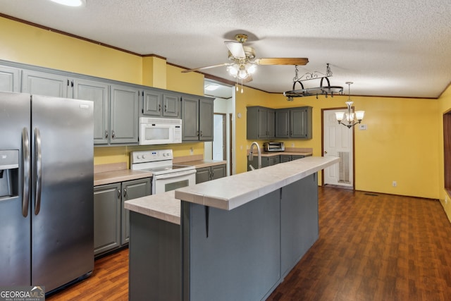 kitchen with white appliances, hanging light fixtures, dark hardwood / wood-style floors, a textured ceiling, and a center island with sink