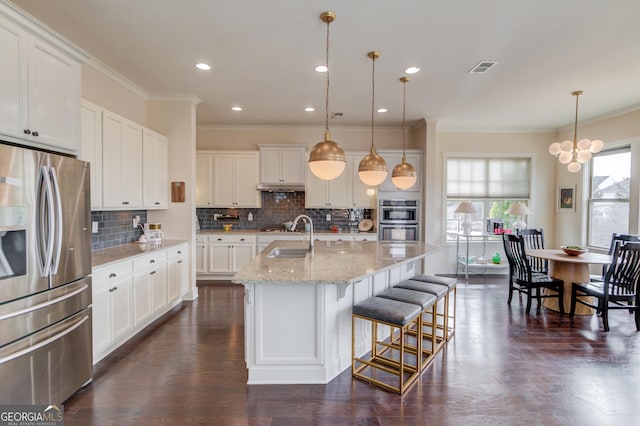 kitchen with pendant lighting, white cabinetry, stainless steel appliances, and an island with sink