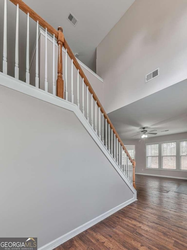 stairs featuring a high ceiling, wood-type flooring, and ceiling fan