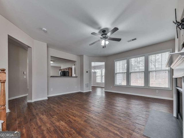 unfurnished living room with ceiling fan with notable chandelier and dark wood-type flooring