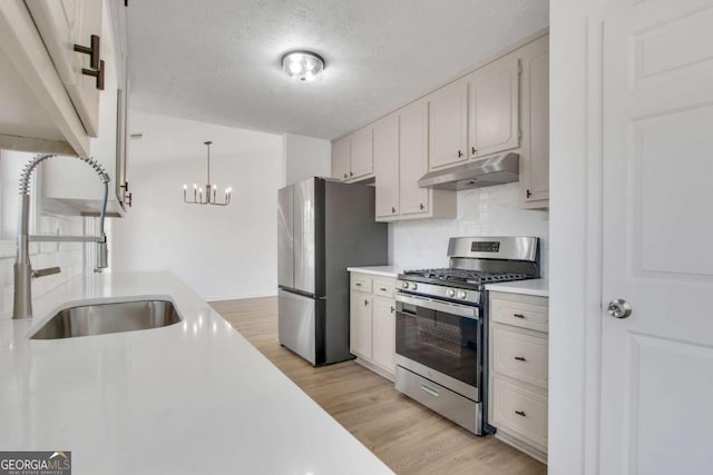 kitchen with appliances with stainless steel finishes, decorative light fixtures, white cabinetry, sink, and light wood-type flooring