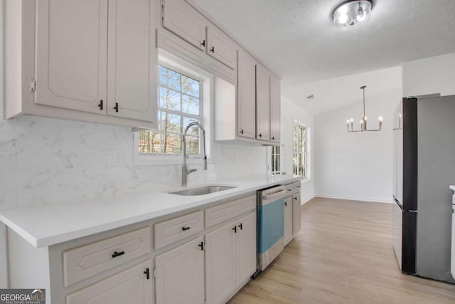 kitchen featuring appliances with stainless steel finishes, sink, white cabinets, hanging light fixtures, and light hardwood / wood-style flooring