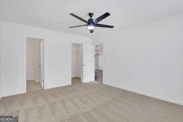 unfurnished bedroom featuring ensuite bathroom, ceiling fan with notable chandelier, a spacious closet, light colored carpet, and a closet