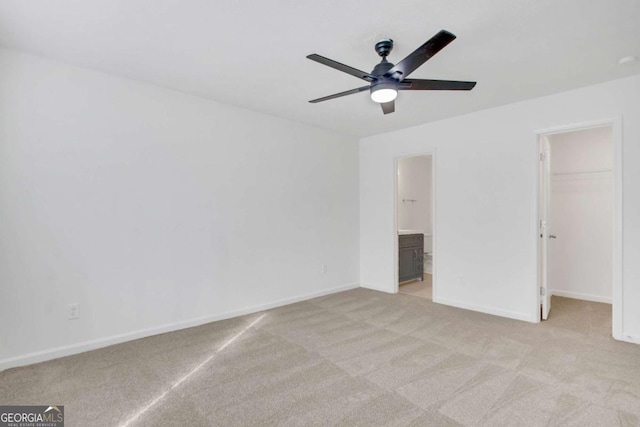 unfurnished bedroom featuring ceiling fan, connected bathroom, light carpet, a spacious closet, and a closet