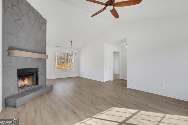 unfurnished living room featuring ceiling fan with notable chandelier, lofted ceiling, a stone fireplace, and light hardwood / wood-style floors