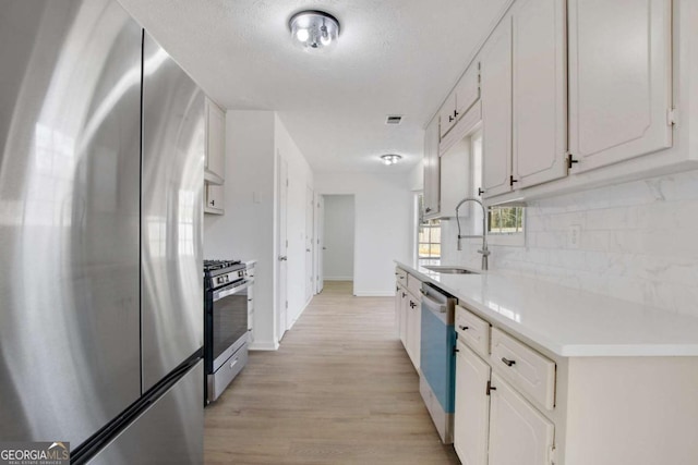 kitchen with sink, appliances with stainless steel finishes, white cabinetry, tasteful backsplash, and light wood-type flooring