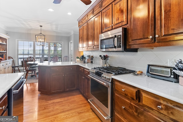 kitchen featuring crown molding, appliances with stainless steel finishes, decorative light fixtures, and light wood-type flooring