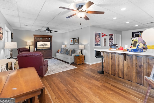 living room with a drop ceiling, hardwood / wood-style floors, and ceiling fan