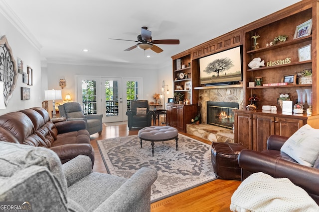 living room featuring a stone fireplace, ornamental molding, ceiling fan, light hardwood / wood-style floors, and french doors