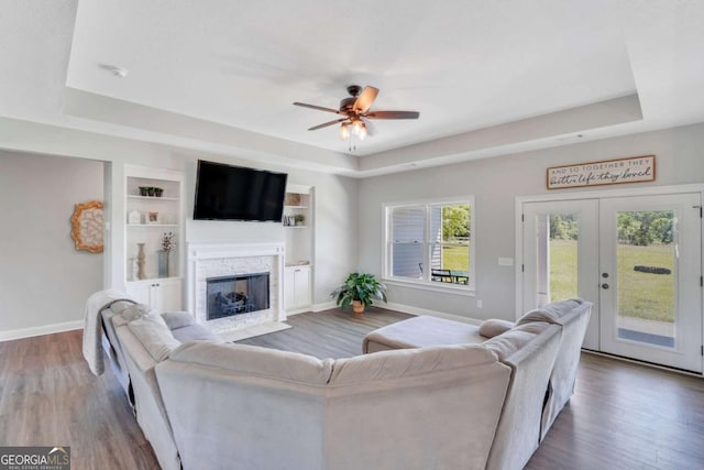 living room with built in shelves, french doors, dark hardwood / wood-style flooring, a raised ceiling, and ceiling fan