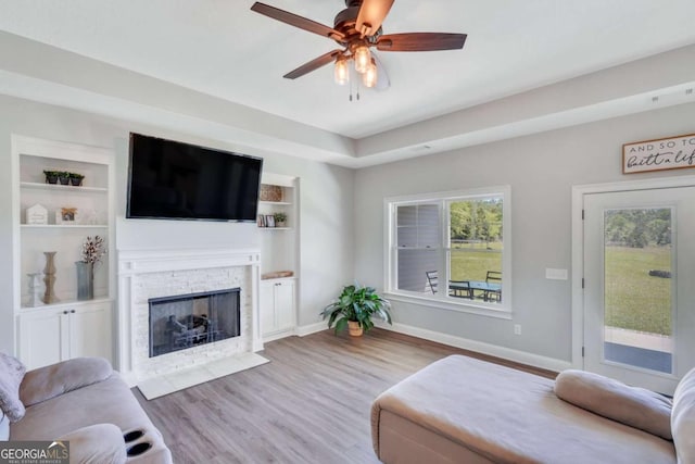 living room featuring ceiling fan, a fireplace, light hardwood / wood-style floors, and built in features