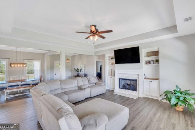 living room featuring wood-type flooring, built in features, and a raised ceiling