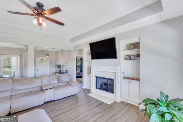 living room with ceiling fan, a tray ceiling, light hardwood / wood-style floors, and built in shelves