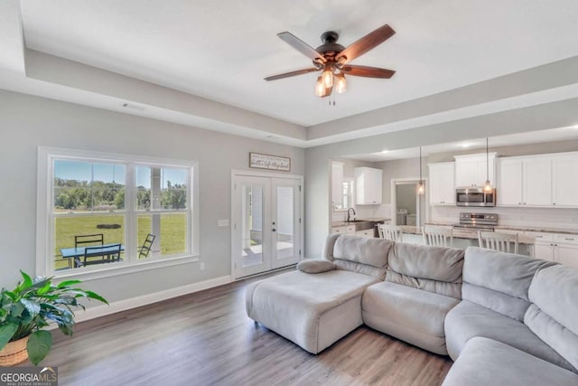 living room with sink, a tray ceiling, light hardwood / wood-style flooring, and ceiling fan