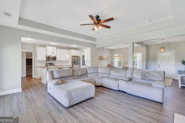 living room featuring a raised ceiling, ceiling fan, and light hardwood / wood-style floors