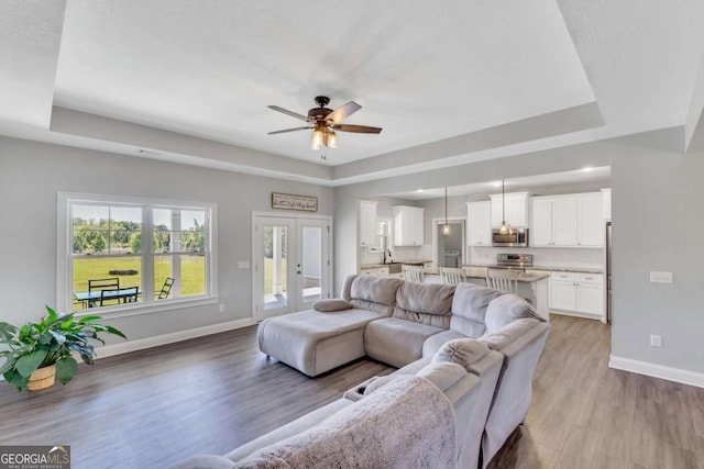 living room featuring french doors, light hardwood / wood-style flooring, ceiling fan, and a tray ceiling