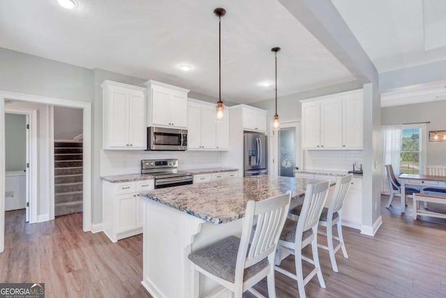 kitchen with stainless steel appliances, a kitchen island, white cabinets, and decorative light fixtures