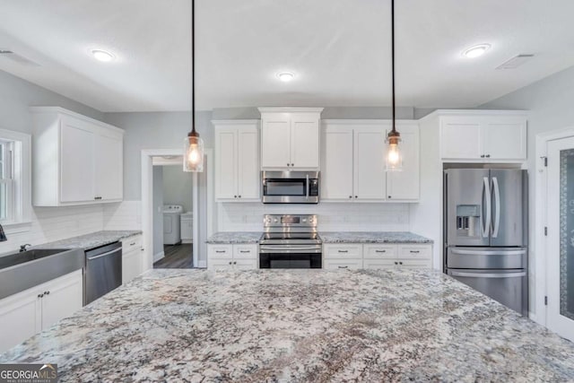 kitchen featuring white cabinetry, hanging light fixtures, stainless steel appliances, independent washer and dryer, and light stone countertops