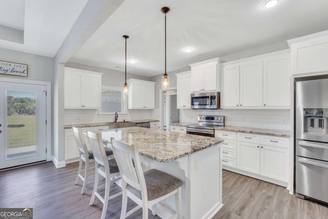 kitchen with white cabinetry, hanging light fixtures, stainless steel appliances, and a kitchen island