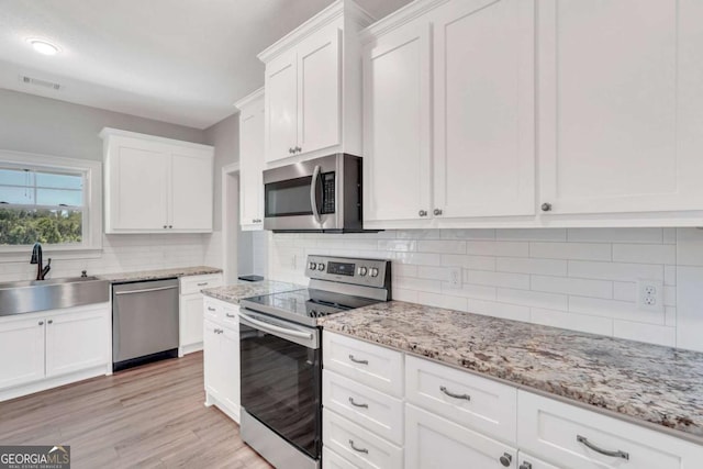 kitchen with sink, appliances with stainless steel finishes, light hardwood / wood-style floors, decorative backsplash, and white cabinets