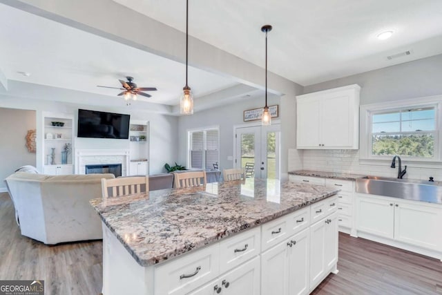 kitchen featuring hanging light fixtures, white cabinetry, a kitchen island, and sink