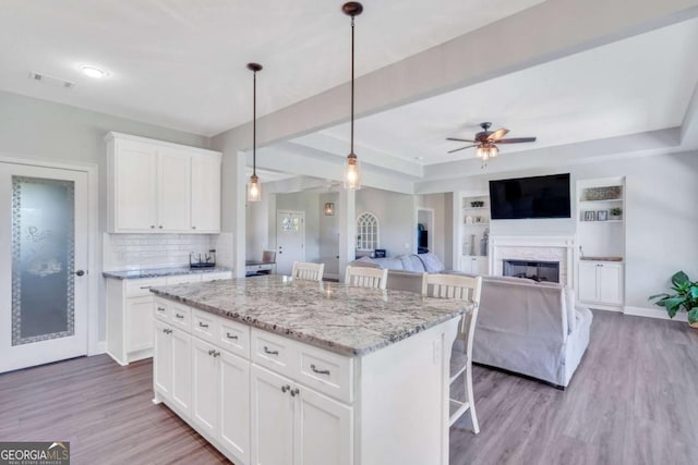 kitchen featuring a kitchen island, decorative light fixtures, white cabinets, a kitchen breakfast bar, and light stone counters