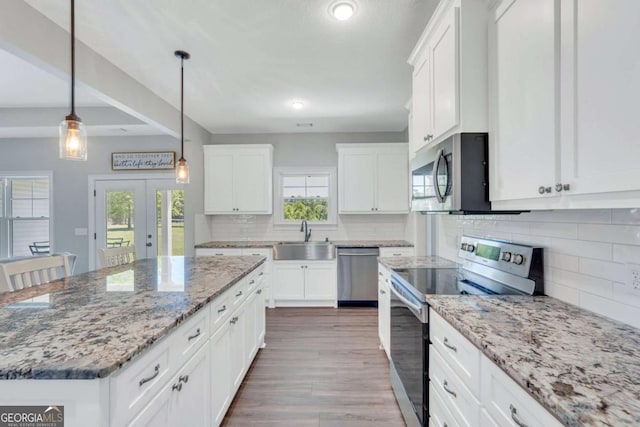 kitchen with decorative light fixtures, stainless steel appliances, white cabinets, and a kitchen island